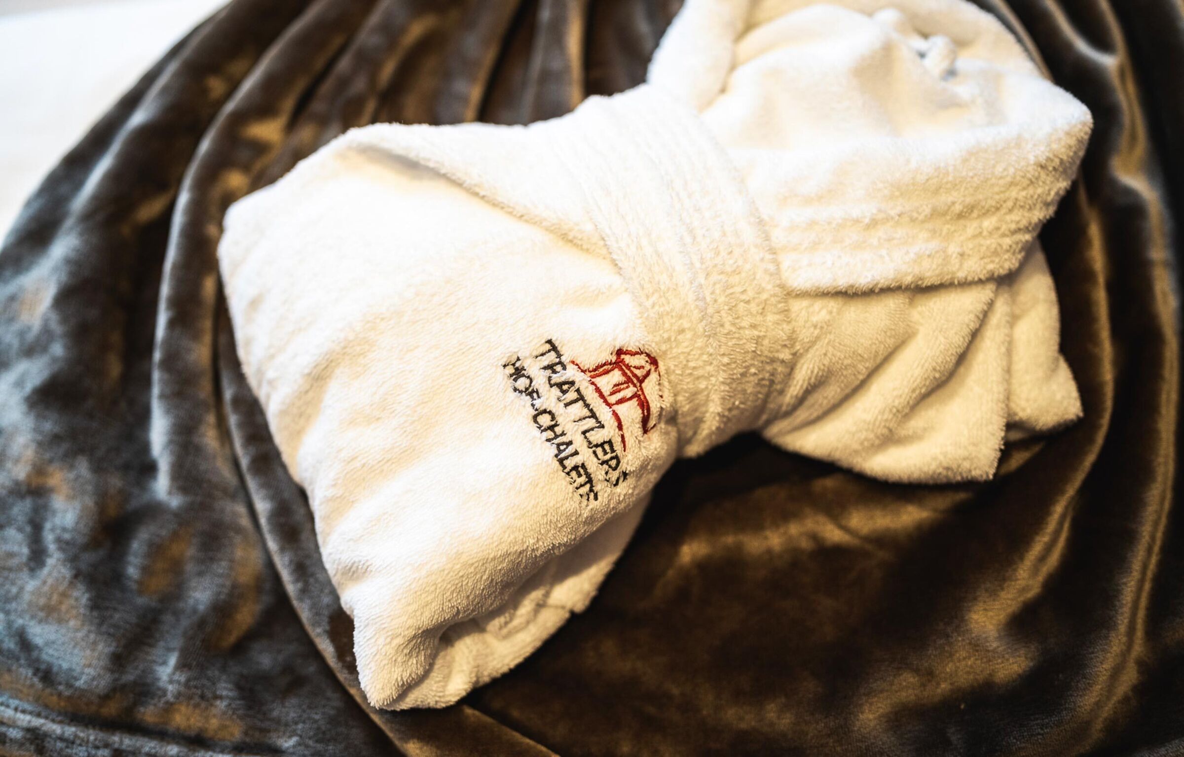 Accappatoio bianco con logo Trattlerhof su coperta vellutata in primo piano.
