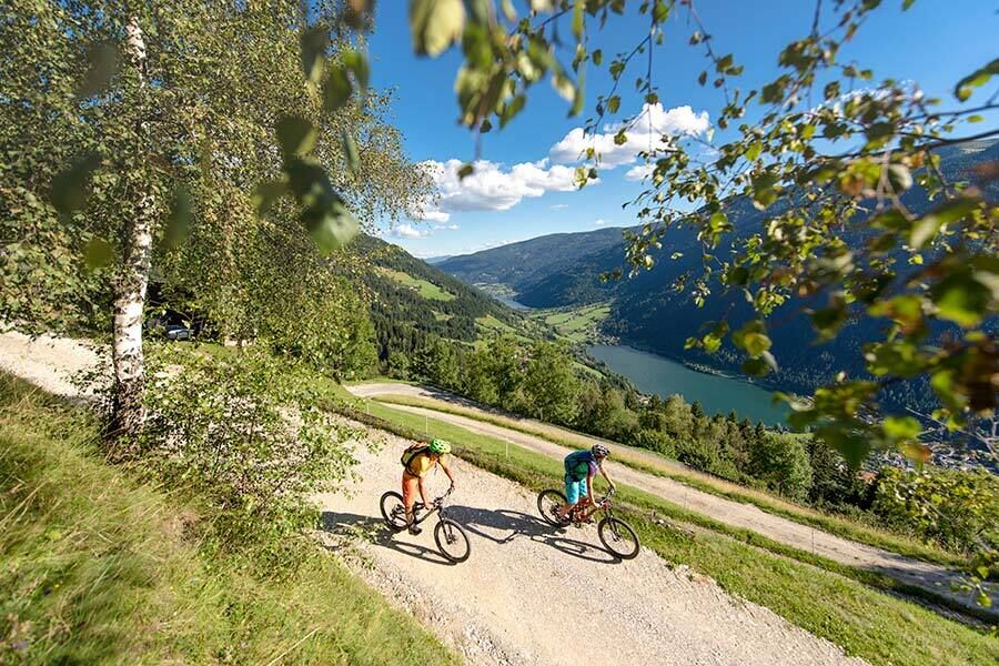 Two cyclists on a mountain path with a breathtaking view of the lake in sunny weather.