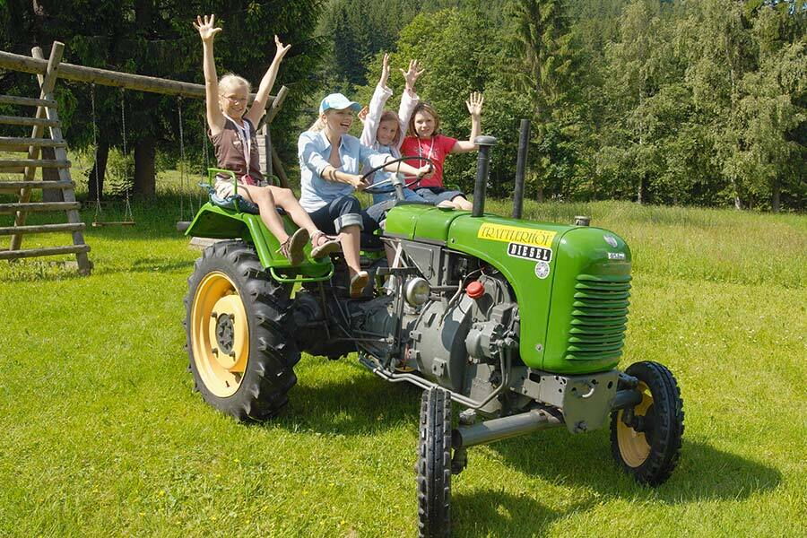 Kinder auf einem grünen Traktor genießen eine Fahrt im Freien bei Sonnenschein.