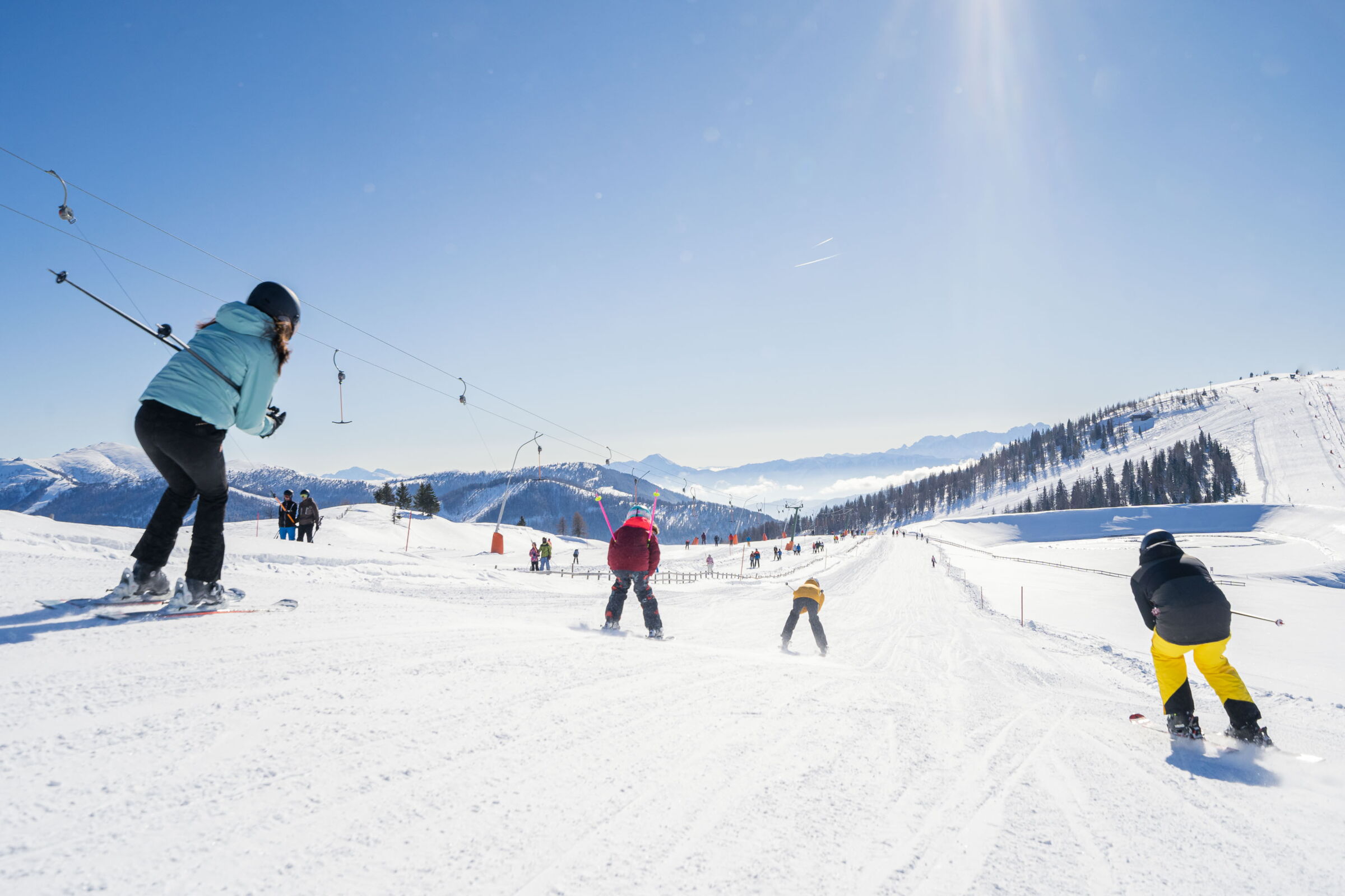 Skiers on a sunny slope with an impressive mountain panorama in the background.