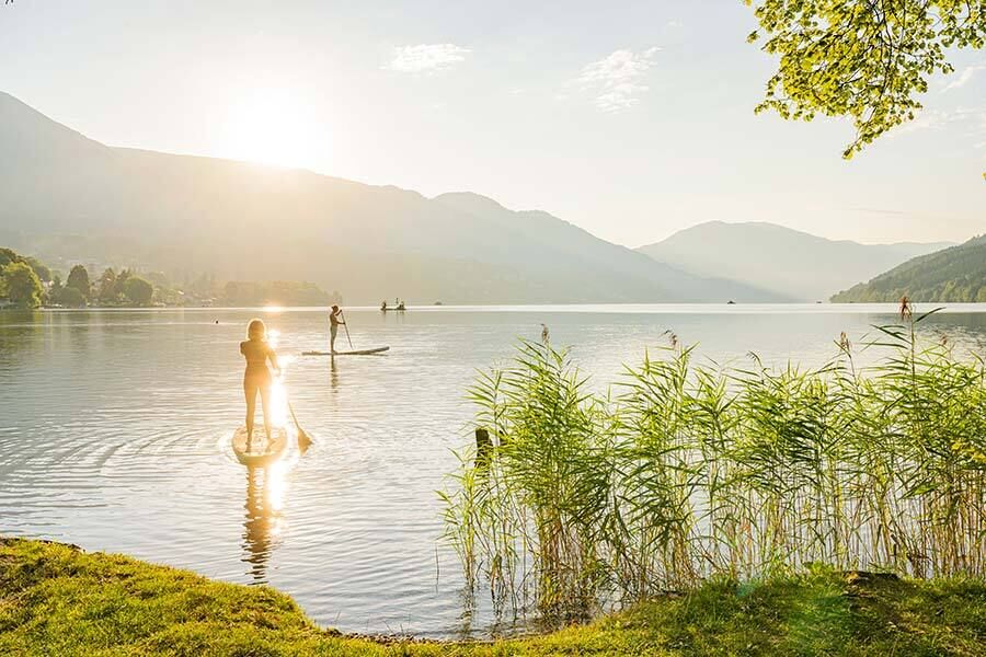 Zwei Personen beim Stand-up-Paddling auf einem See in sonniger Berglandschaft.