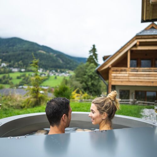 Paar genießt Whirlpool mit Bergblick und Champagner bei Holzchalet.