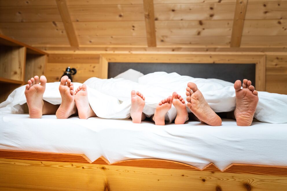 Four feet of adults and two of children under a blanket in a wooden bed.