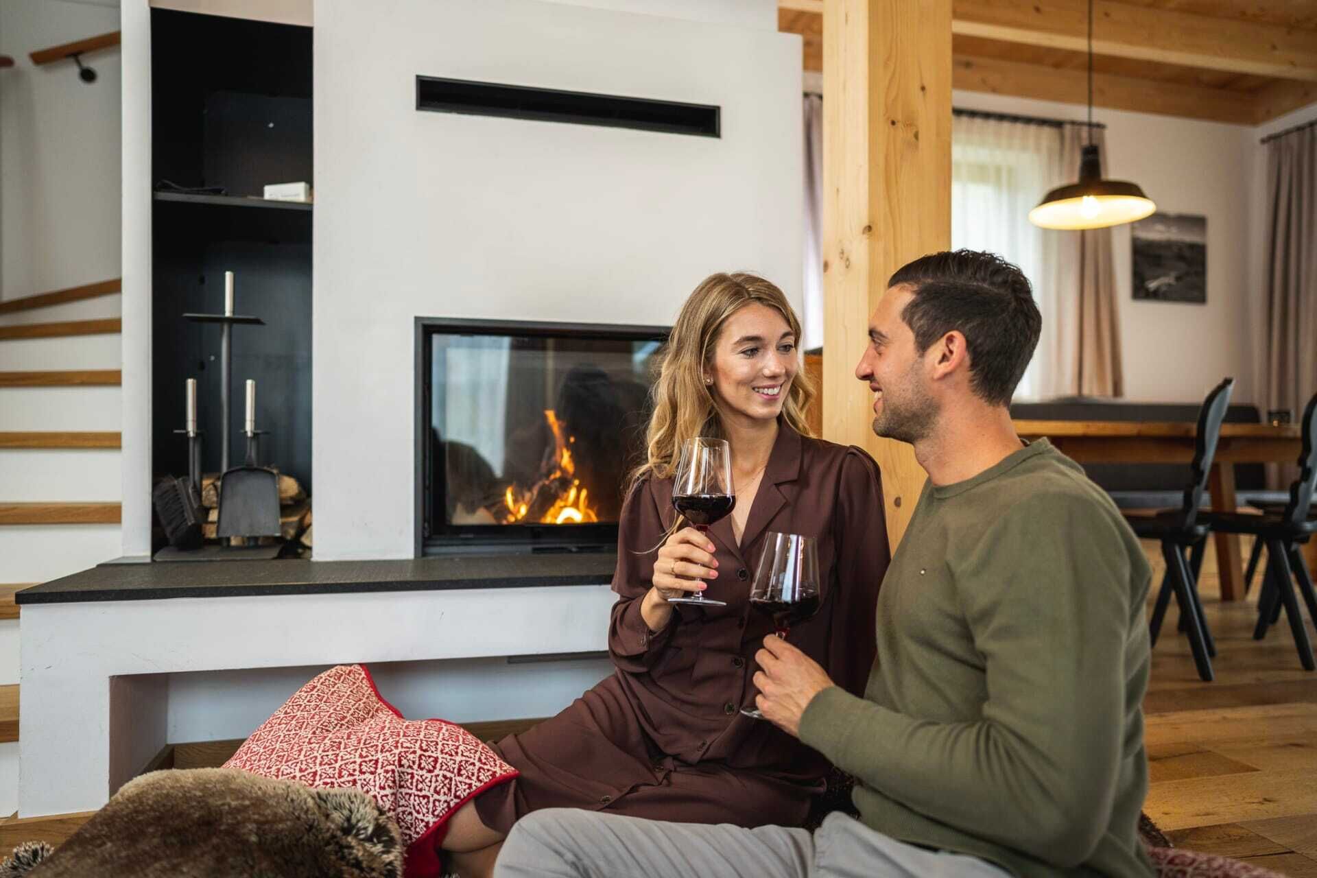 Couple enjoys wine in front of the fireplace in a cozy chalet ambience