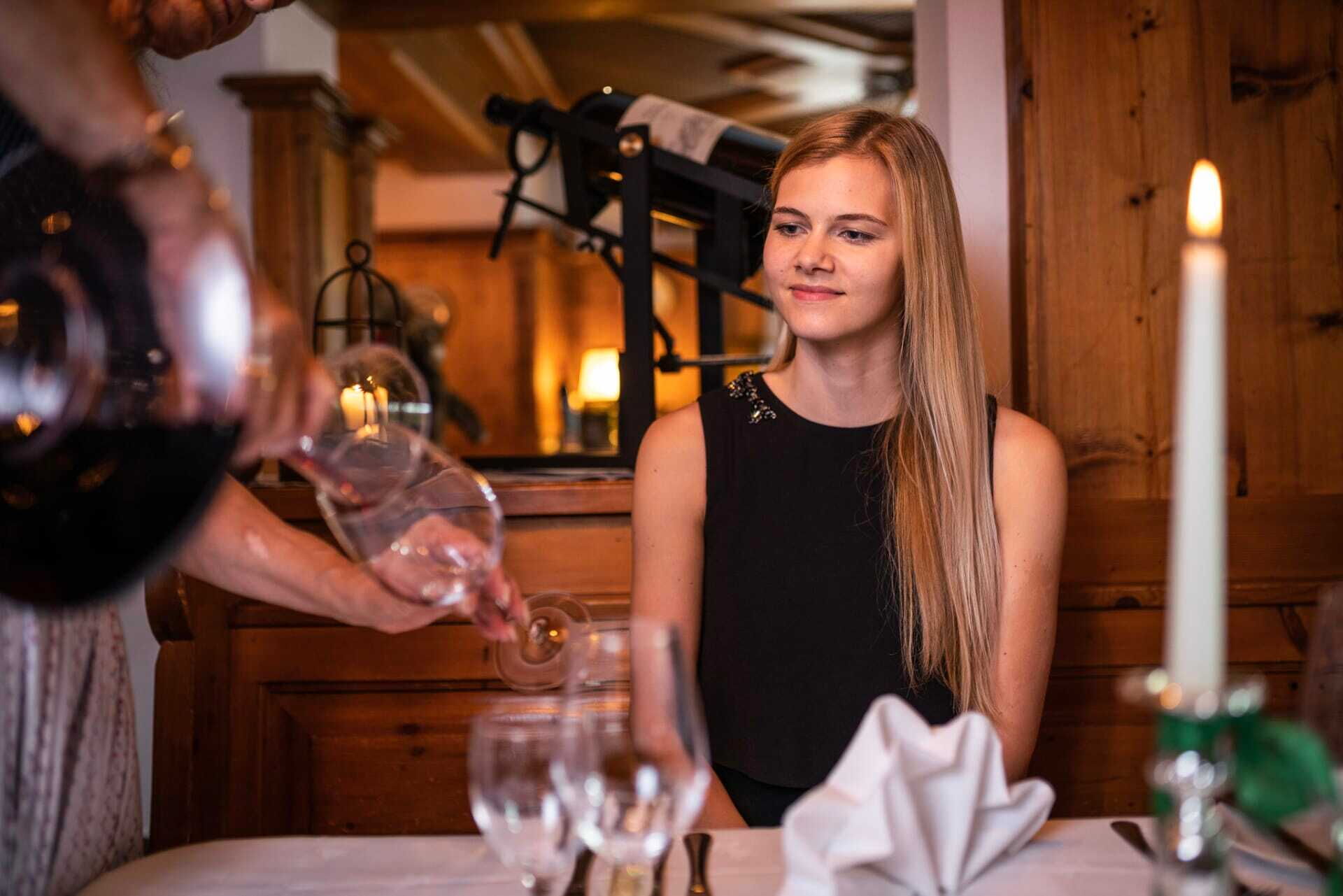 Frau genießt Wein in gemütlicher Chalet-Atmosphäre mit Kerzenlicht und Holzinterieur.