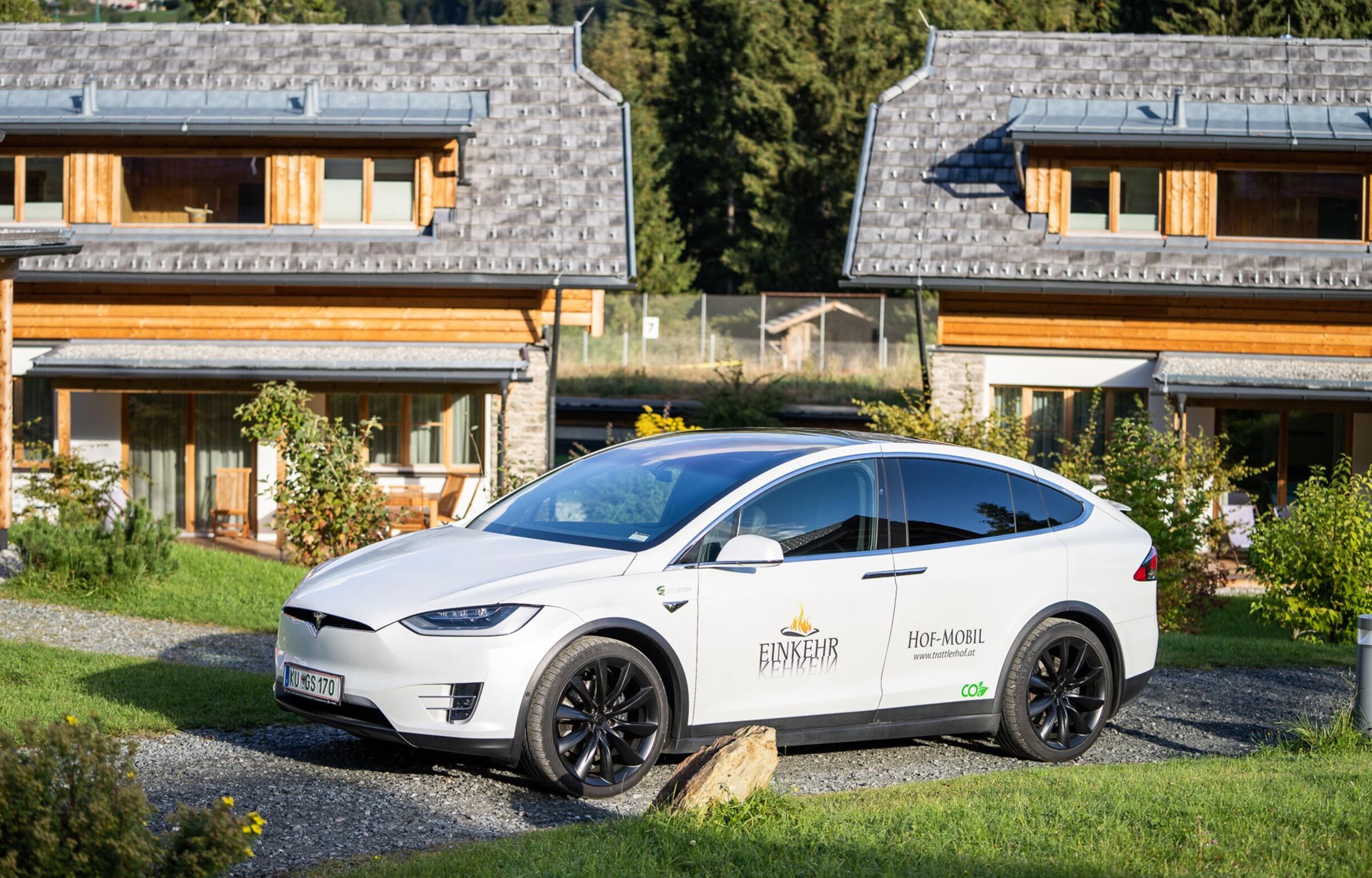 Weißer Tesla vor traditionellen Chalets in grüner, idyllischer Umgebung.