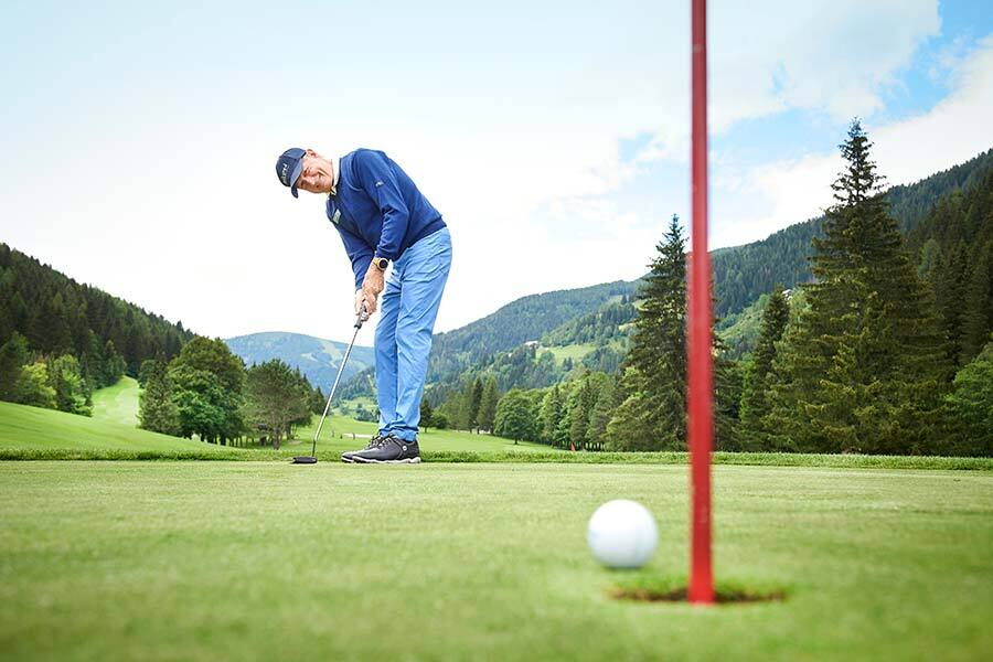 Golfers putting on a well-tended green, surrounded by a picturesque mountain landscape.