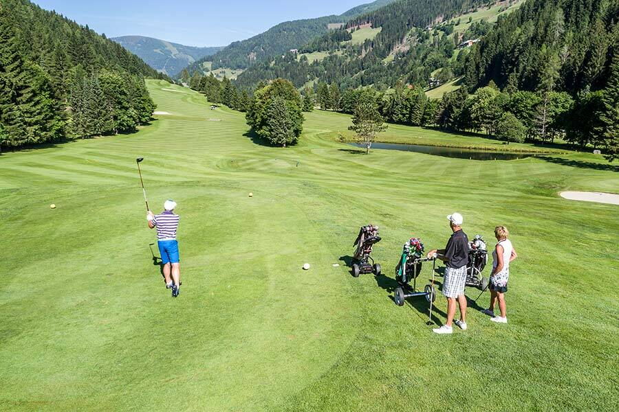 Golfer schlagen auf grünen Fairways in malerischer Berglandschaft ab.