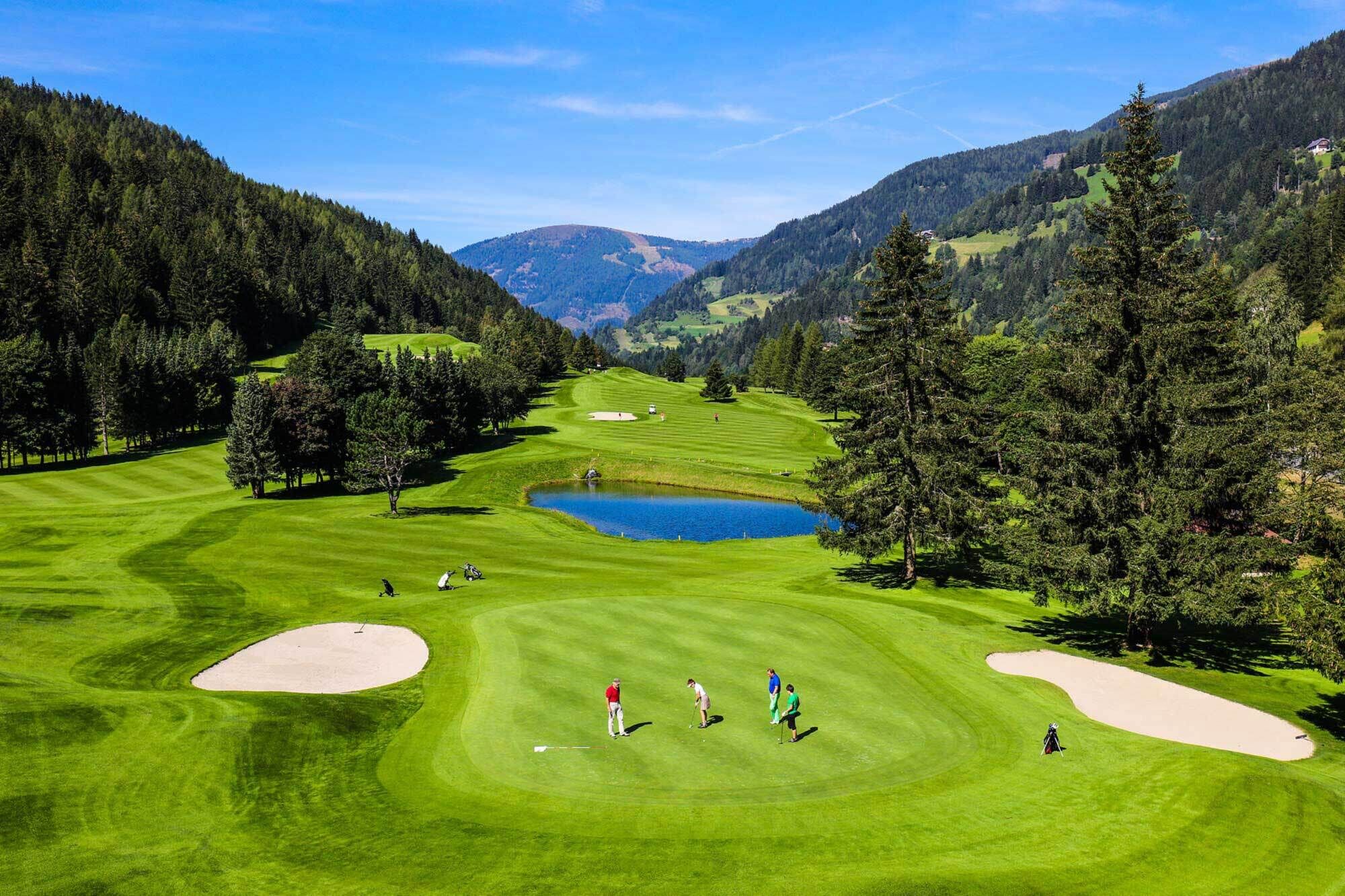 Green fairways and golfers in a picturesque mountain landscape with a pond