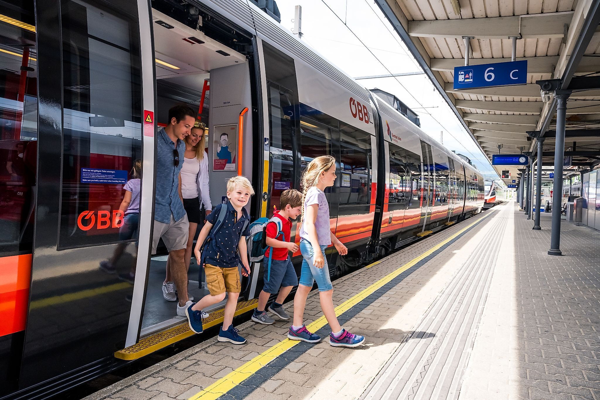 Una famiglia scende da un treno moderno in una giornata di sole.