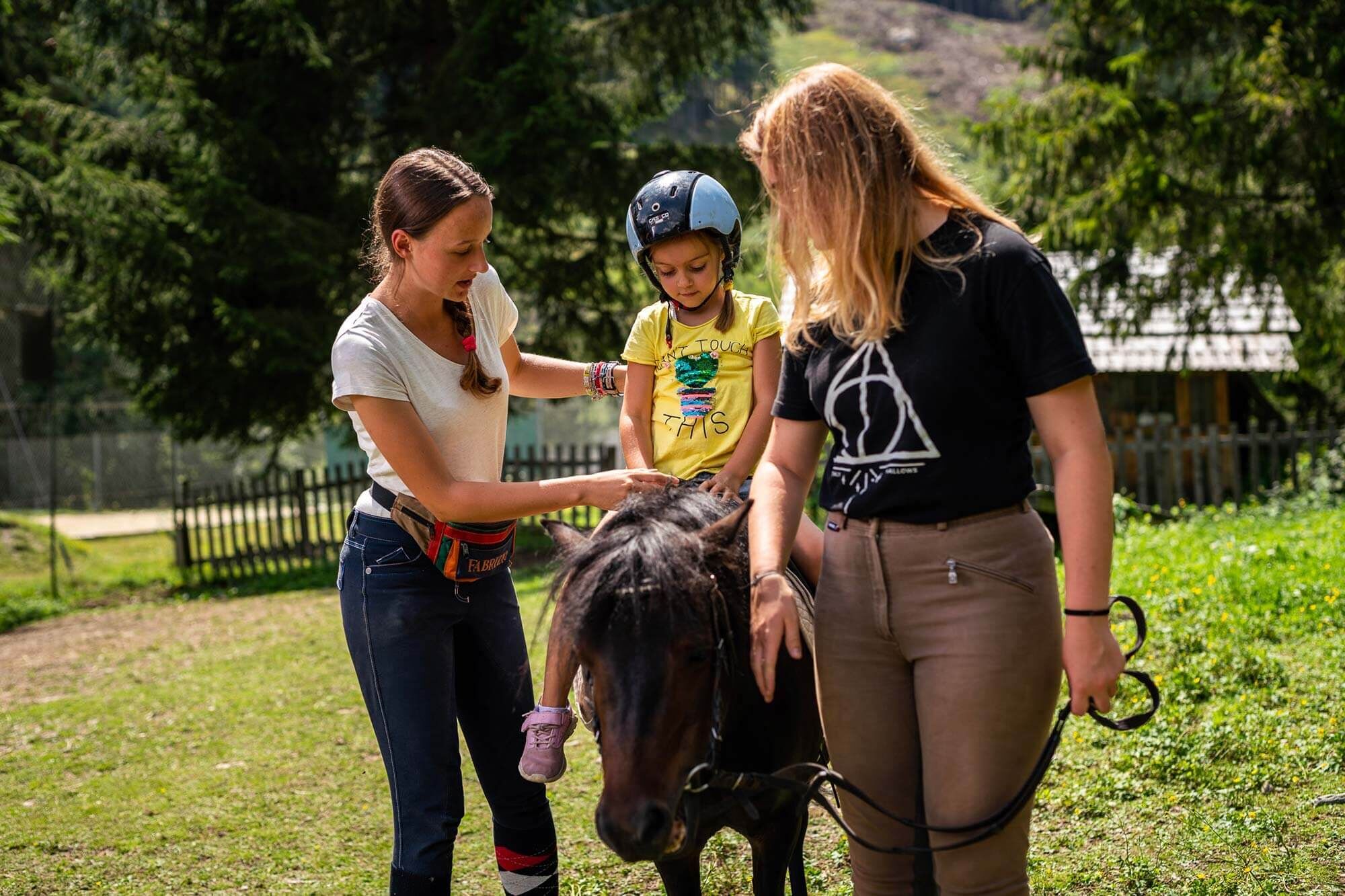Kind beim Ponyreiten von zwei Erwachsenen betreut, im Grünen, sonniger Tag.