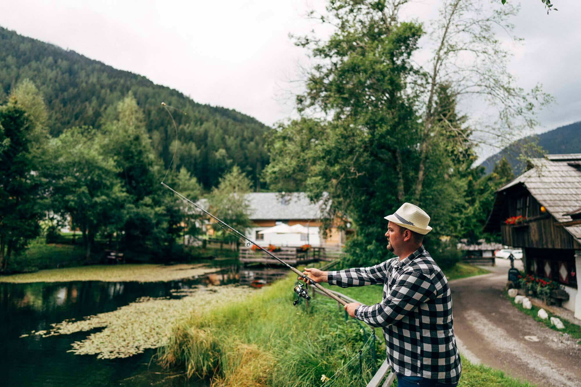A person fishing at a quiet lake with surrounding forest landscape in Carinthia.