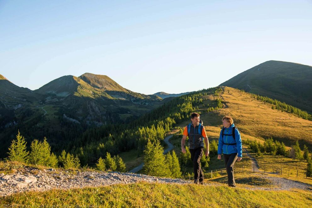 Zwei Wanderer auf einem Pfad in den sonnigen Nockbergen mit weitem Bergblick.