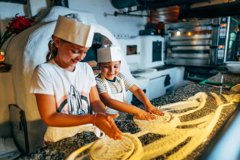 Due bambini modellano felicemente l'impasto della pizza in una cucina accogliente.