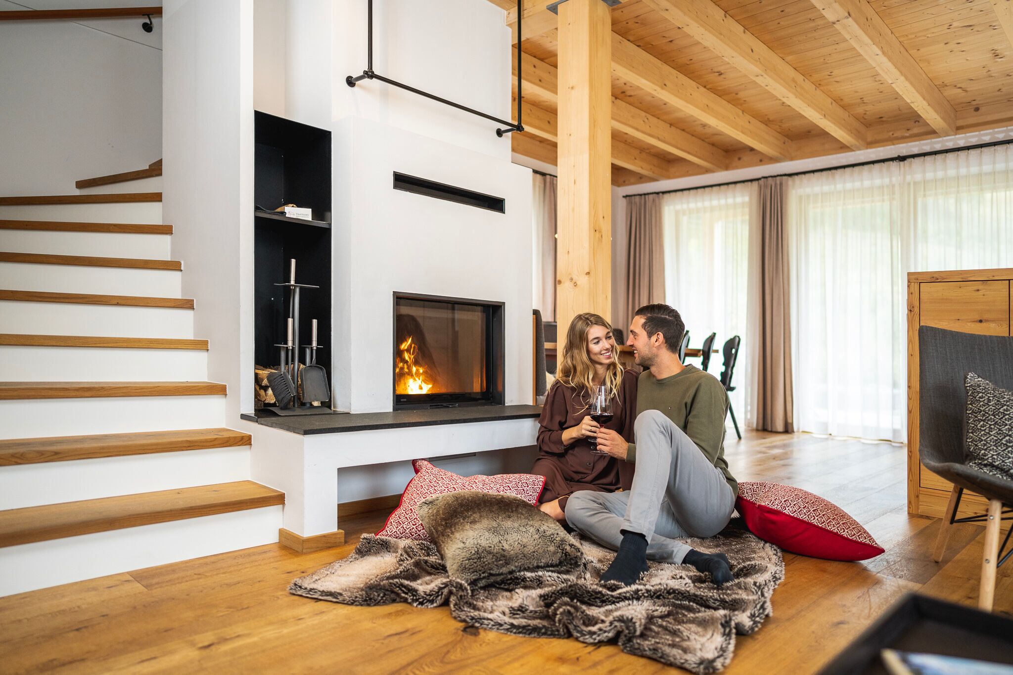 Couple relaxing in front of the fireplace in a cozy chalet with rustic wooden furnishings.