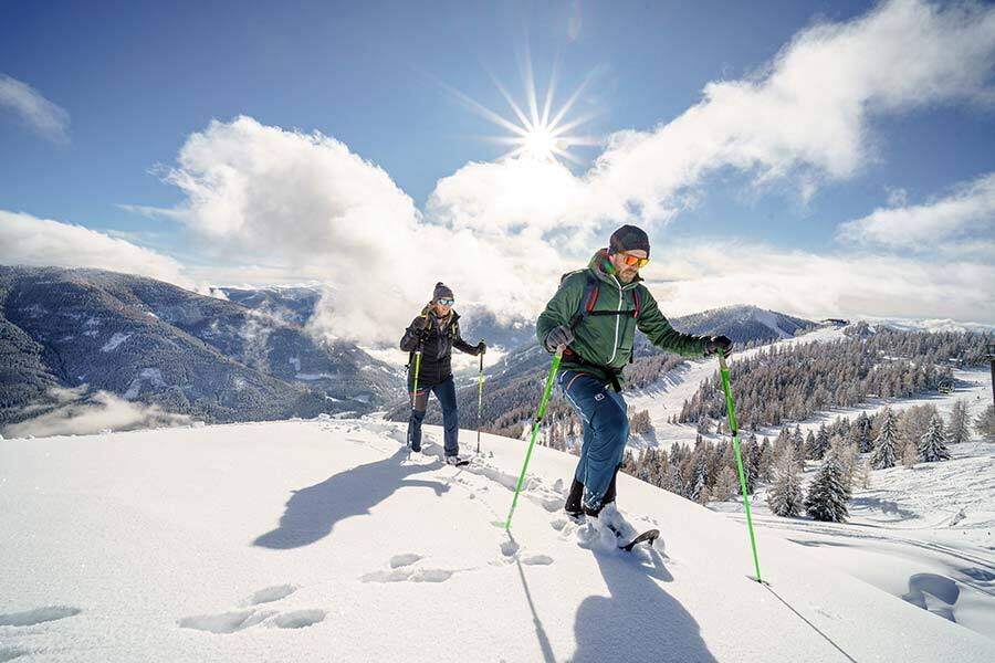 Two people hiking with snowshoes in the sunny, snow-covered mountain panorama of Carinthia.
