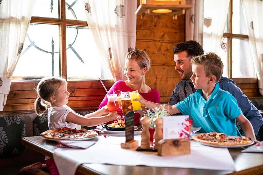 Familie genießt gemeinsames Essen in gemütlichem Chalet mit Pizza und Getränken.