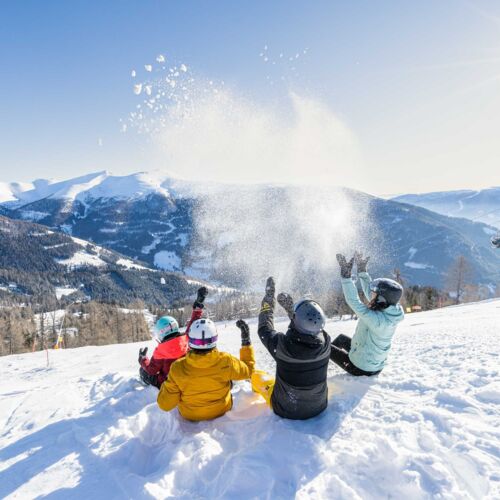 Family playing in the snow with a mountain view under a bright winter sun.