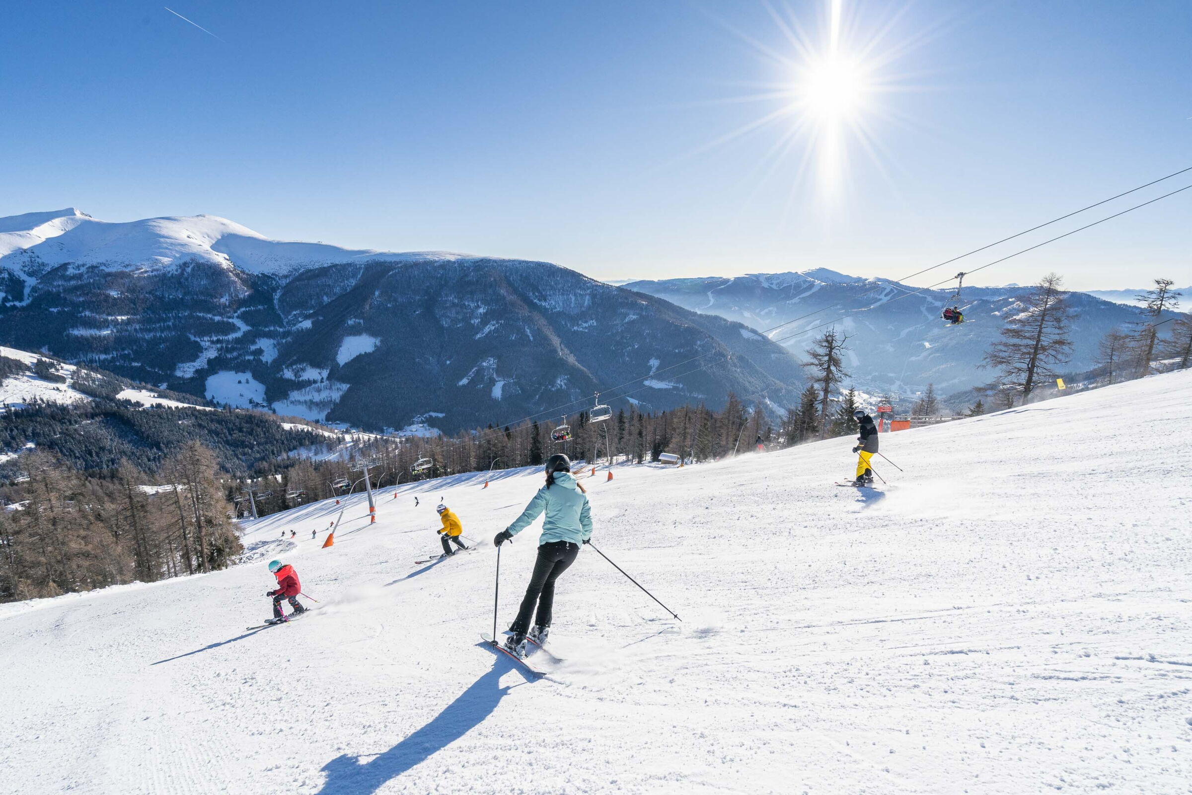 Skifahrer genießen sonnigen Tag auf breiter Skipiste mit majestätischen Bergblicken.