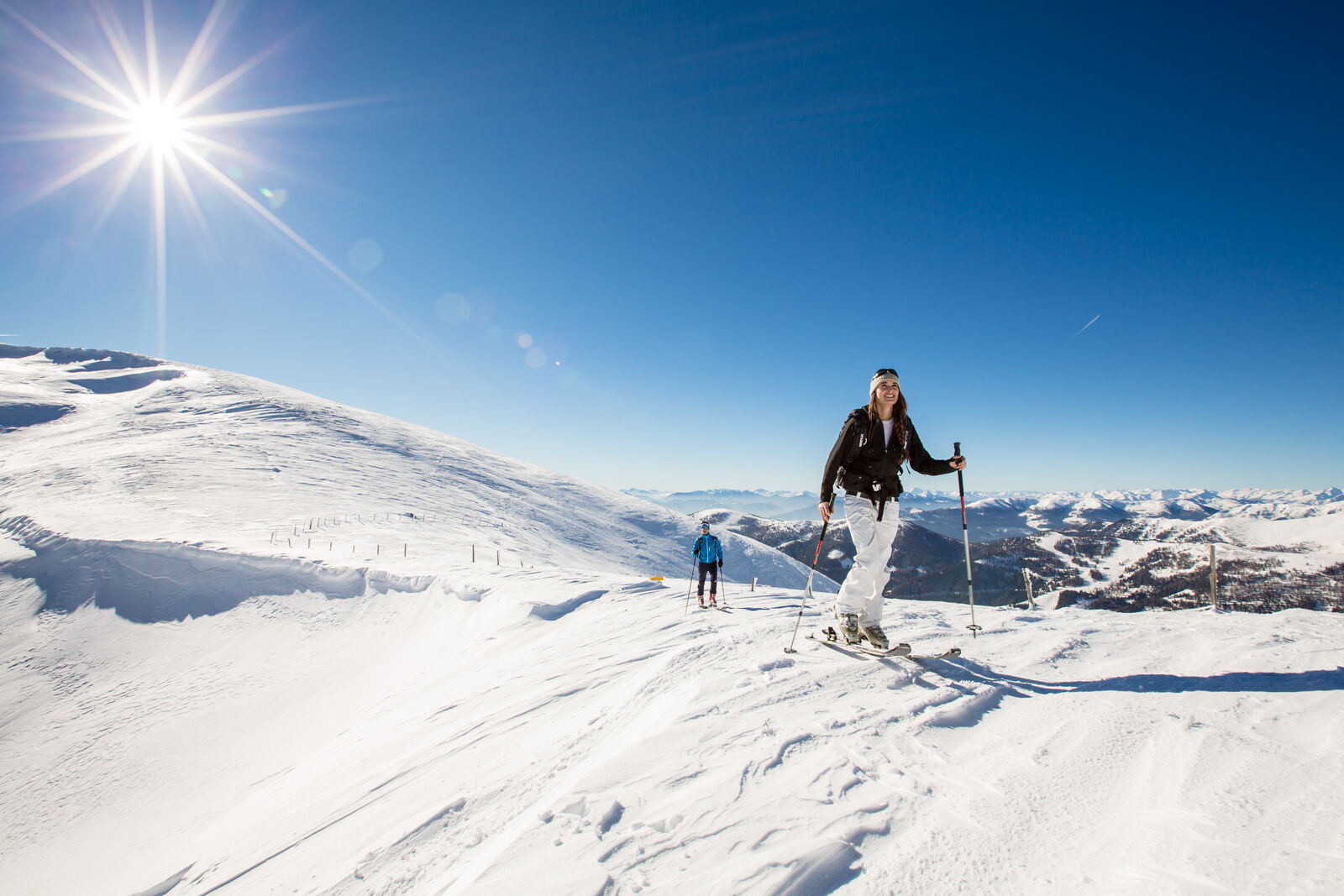 Zwei Personen auf Skitour bei strahlendem Sonnenschein in den verschneiten Nockbergen.