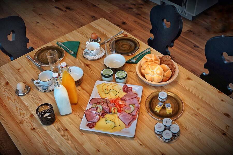 Un tavolo per la colazione con panini, salumi, formaggi, uova e bevande.