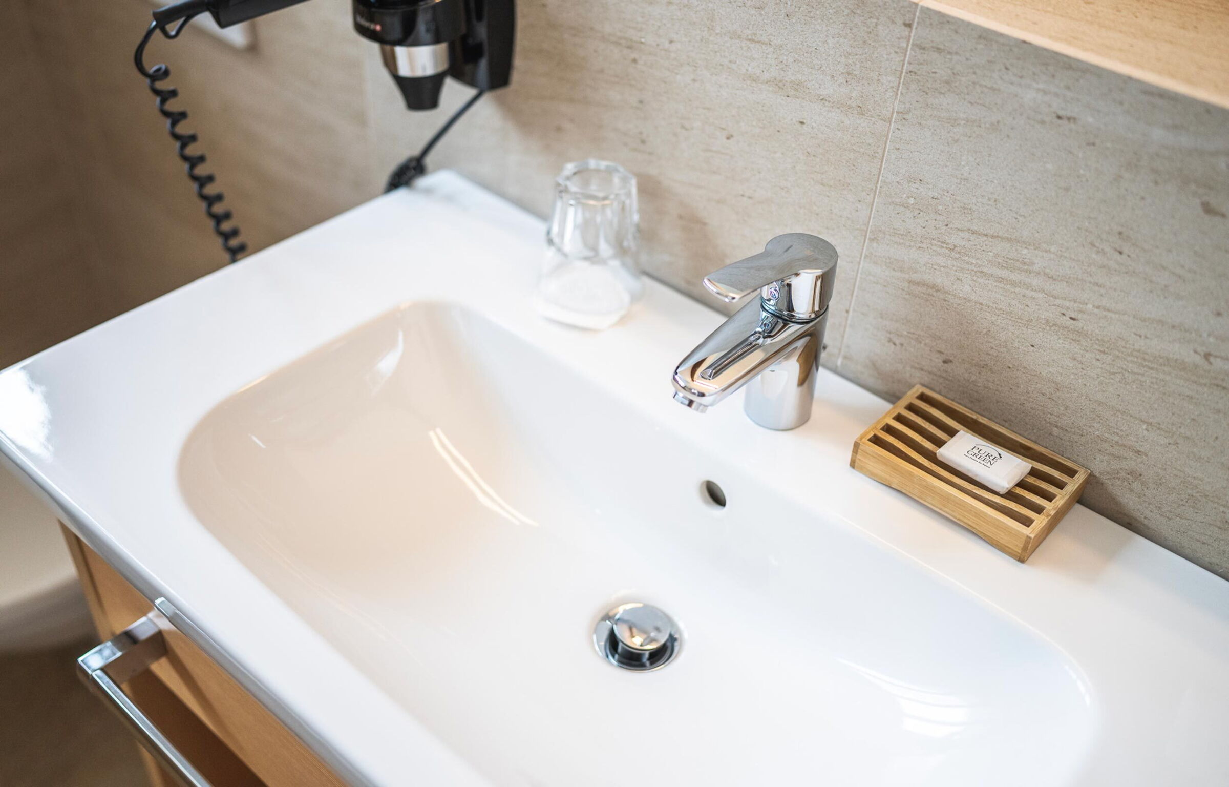 Lavabo moderno con rubinetto lucido e portasapone in legno in un bagno.