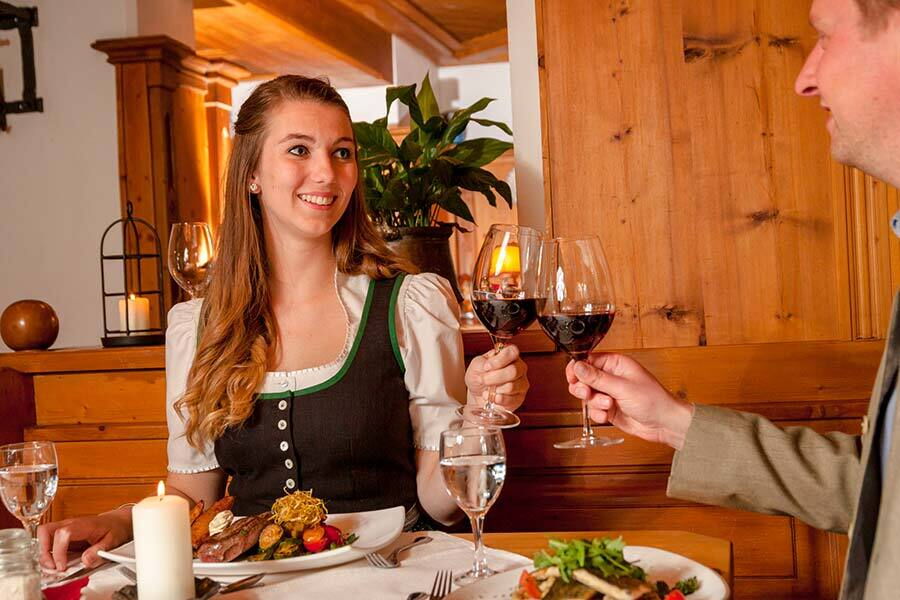 Two people clink glasses of red wine by candlelight at a festively laid table.
