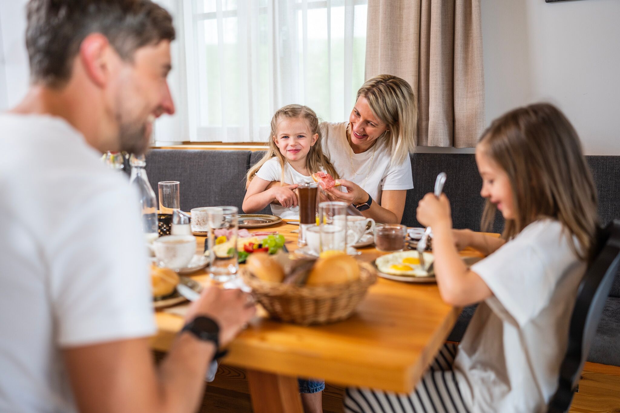 Familie genießt gemeinsames Frühstück in gemütlicher Chalet-Atmosphäre, strahlende Gesichter am Tisch.