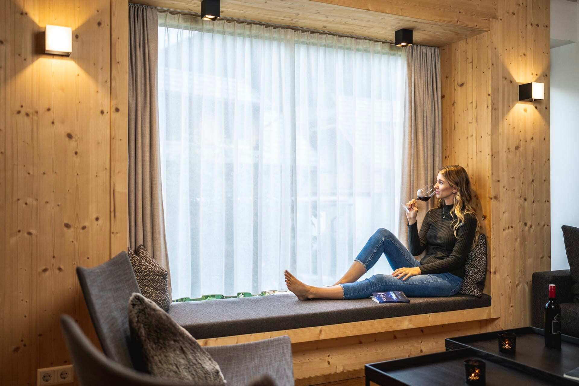 Woman enjoying wine on a windowsill in a cozy chalet with wood paneling.