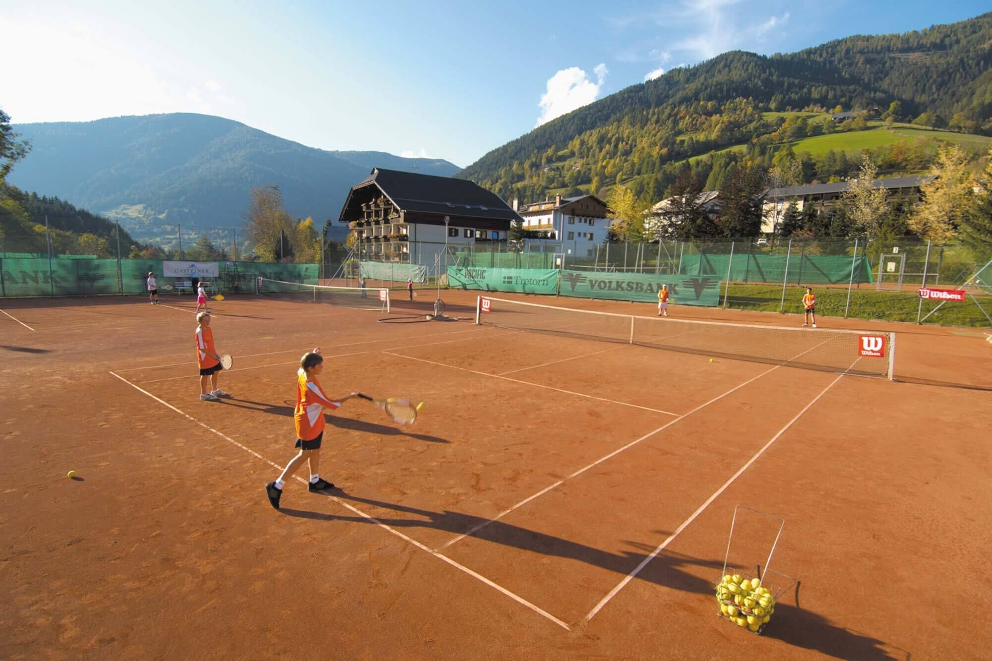 Tennisplatz mit Spielern und malerischem Bergpanorama im Hintergrund.