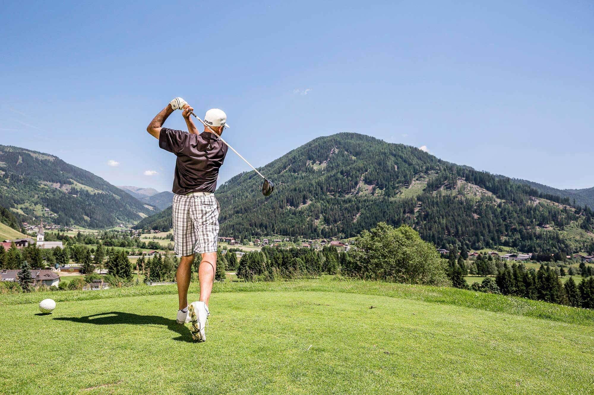Golfer beim Abschlag auf grünem Fairway, umgeben von malerischen Bergen.