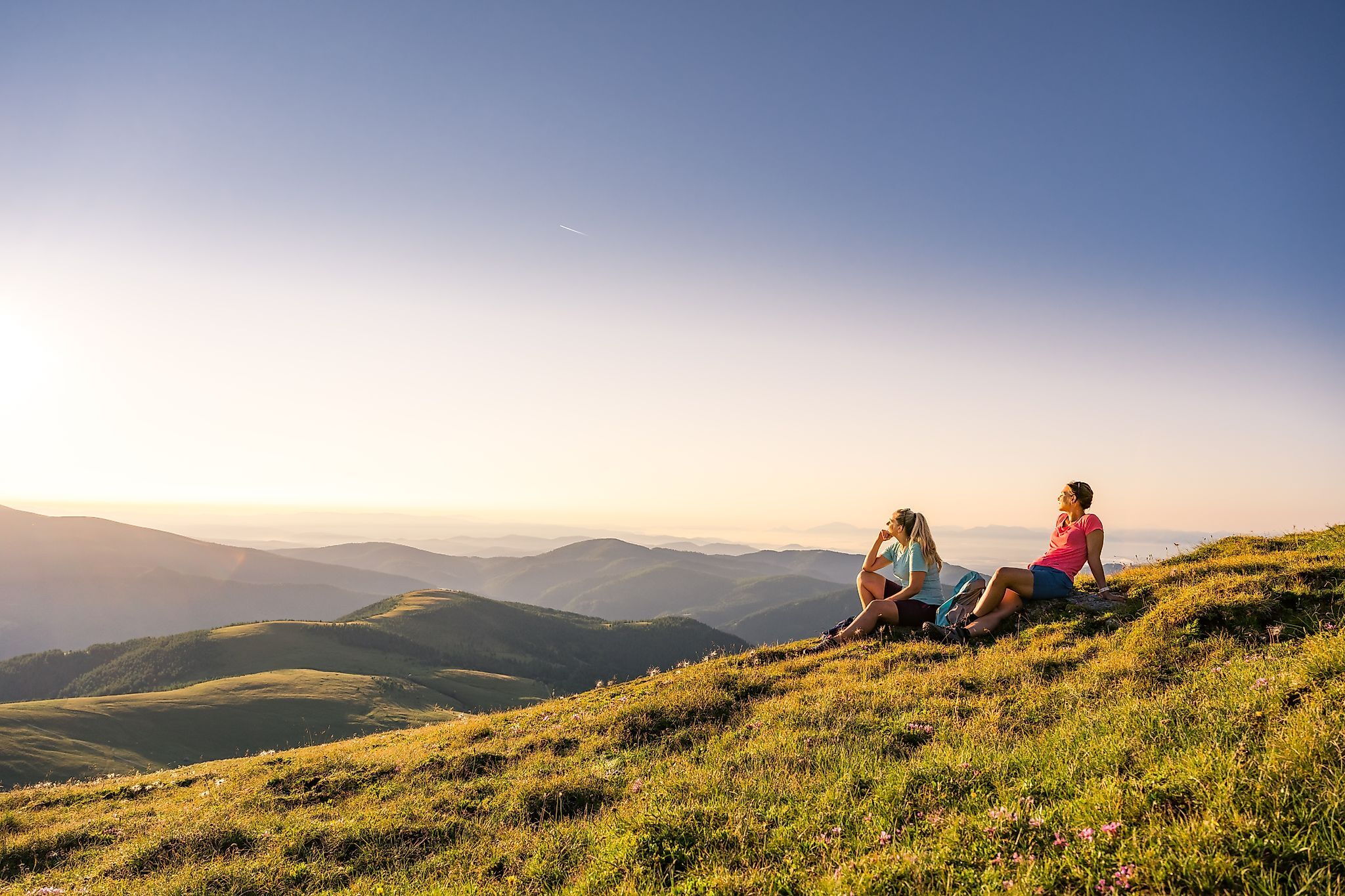 Two people enjoy the sunset on a mountain meadow with a sweeping view.