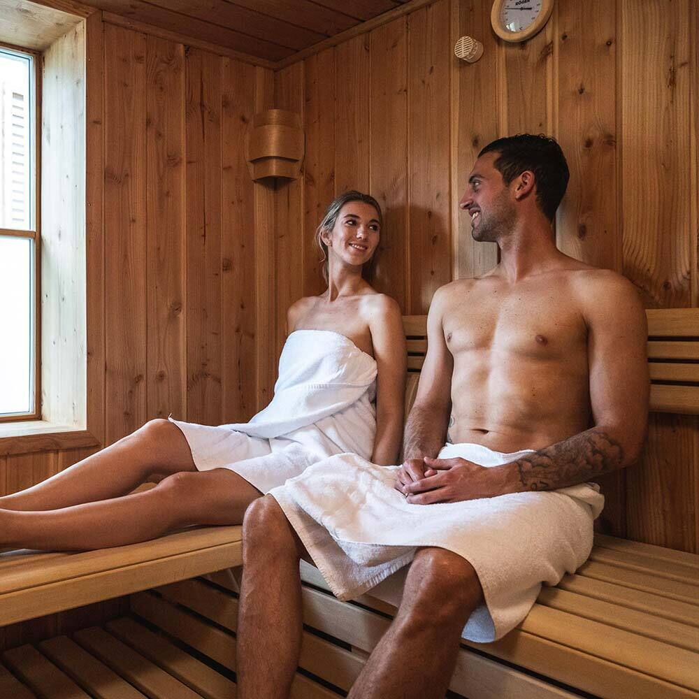 Paar entspannt in einer hölzernen Sauna mit warmem Licht und Fenster.
