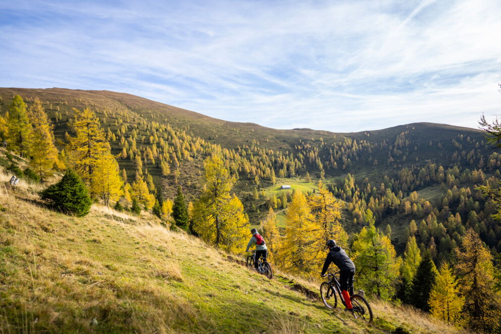 Zwei Radfahrer genießen eine Fahrt durch die herbstliche Landschaft der Nockberge.