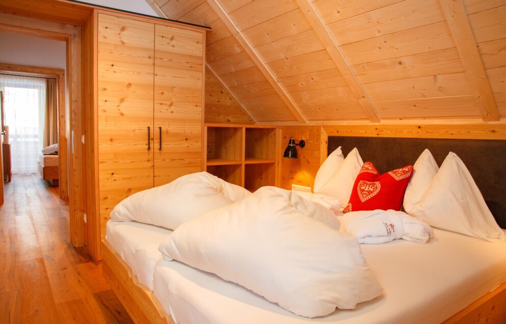 Kuscheliges Bett in einem Chaletzimmer mit Holzwänden und roten Dekokissen.