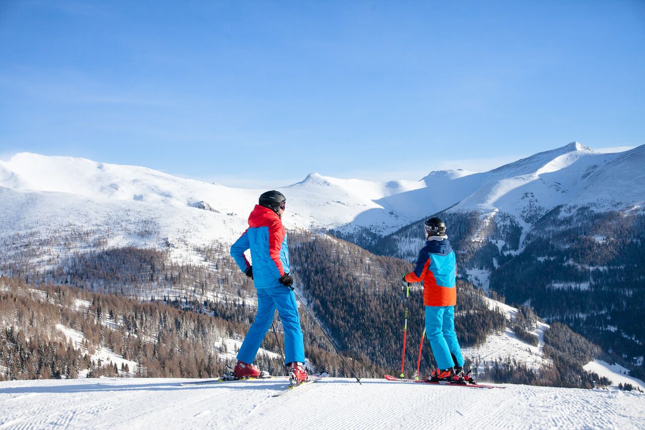 Zwei Skifahrer genießen den atemberaubenden Blick auf schneebedeckte Berge und Wälder.