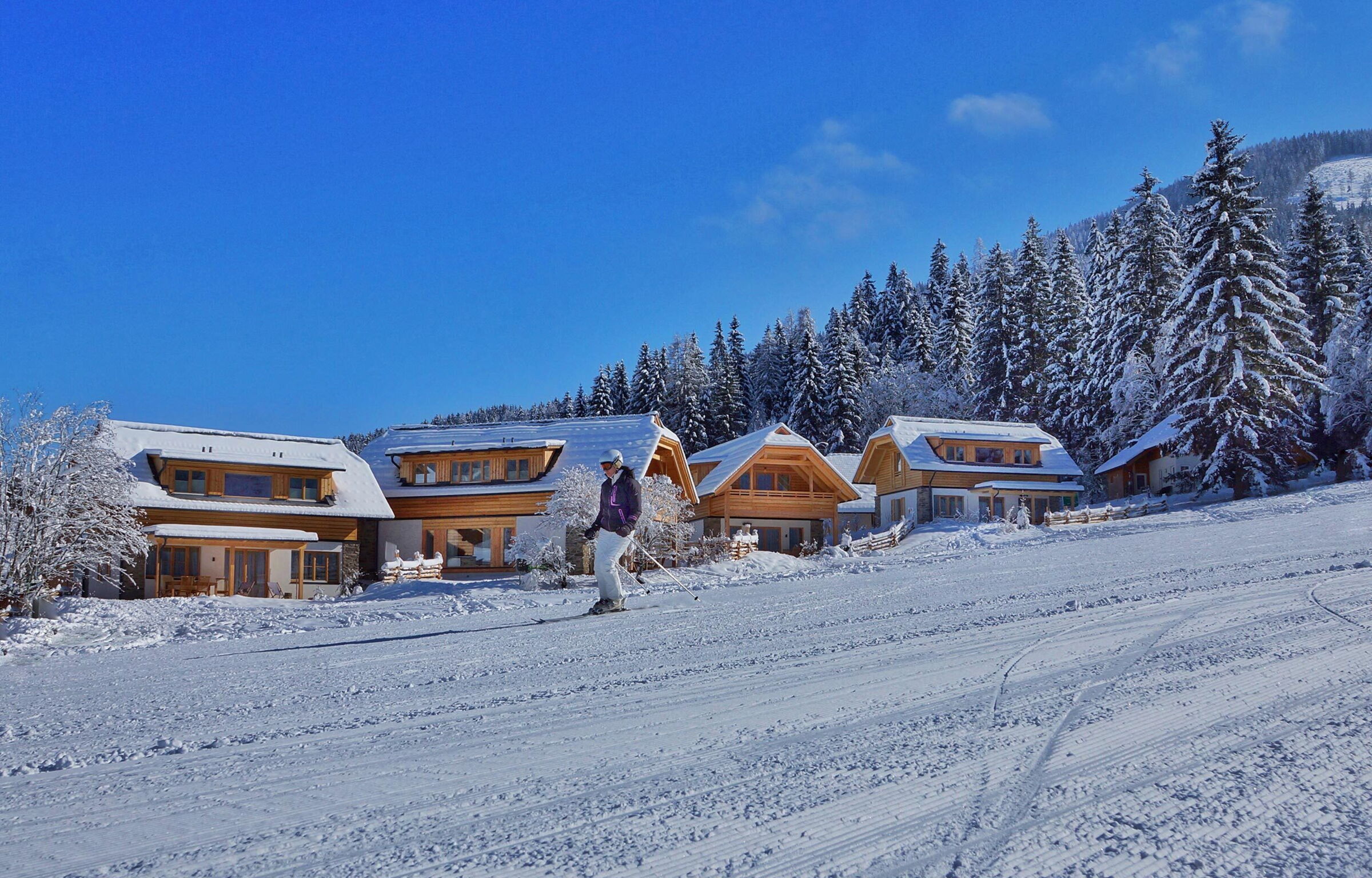 Skifahrer vor schneebedeckten, gemütlichen Chalets in sonniger Winterlandschaft.