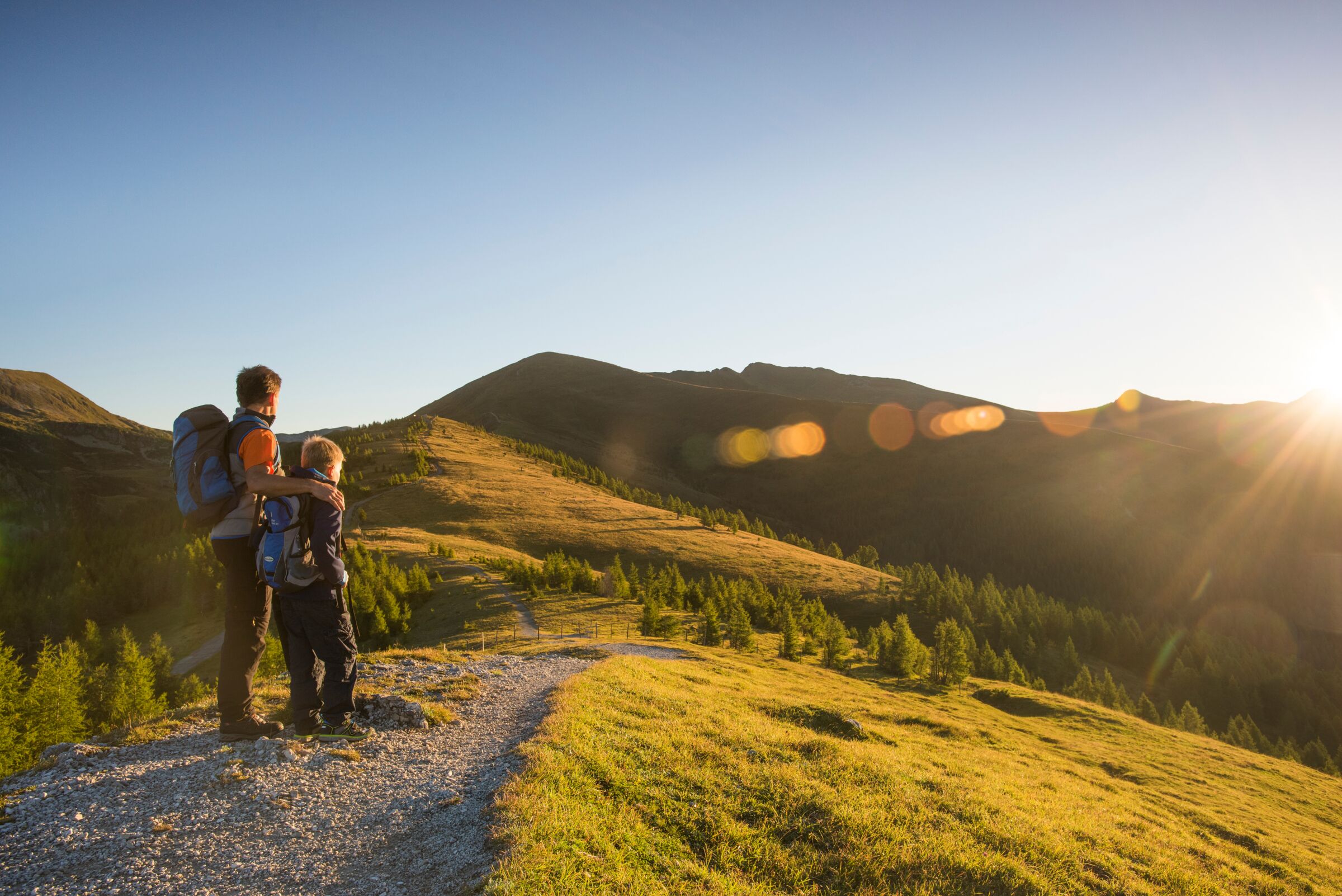 Father and son enjoy the panorama in a sunny mountain landscape at sunrise.
