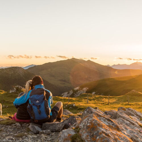Una coppia si gode il tramonto in montagna accanto a mucche al pascolo.