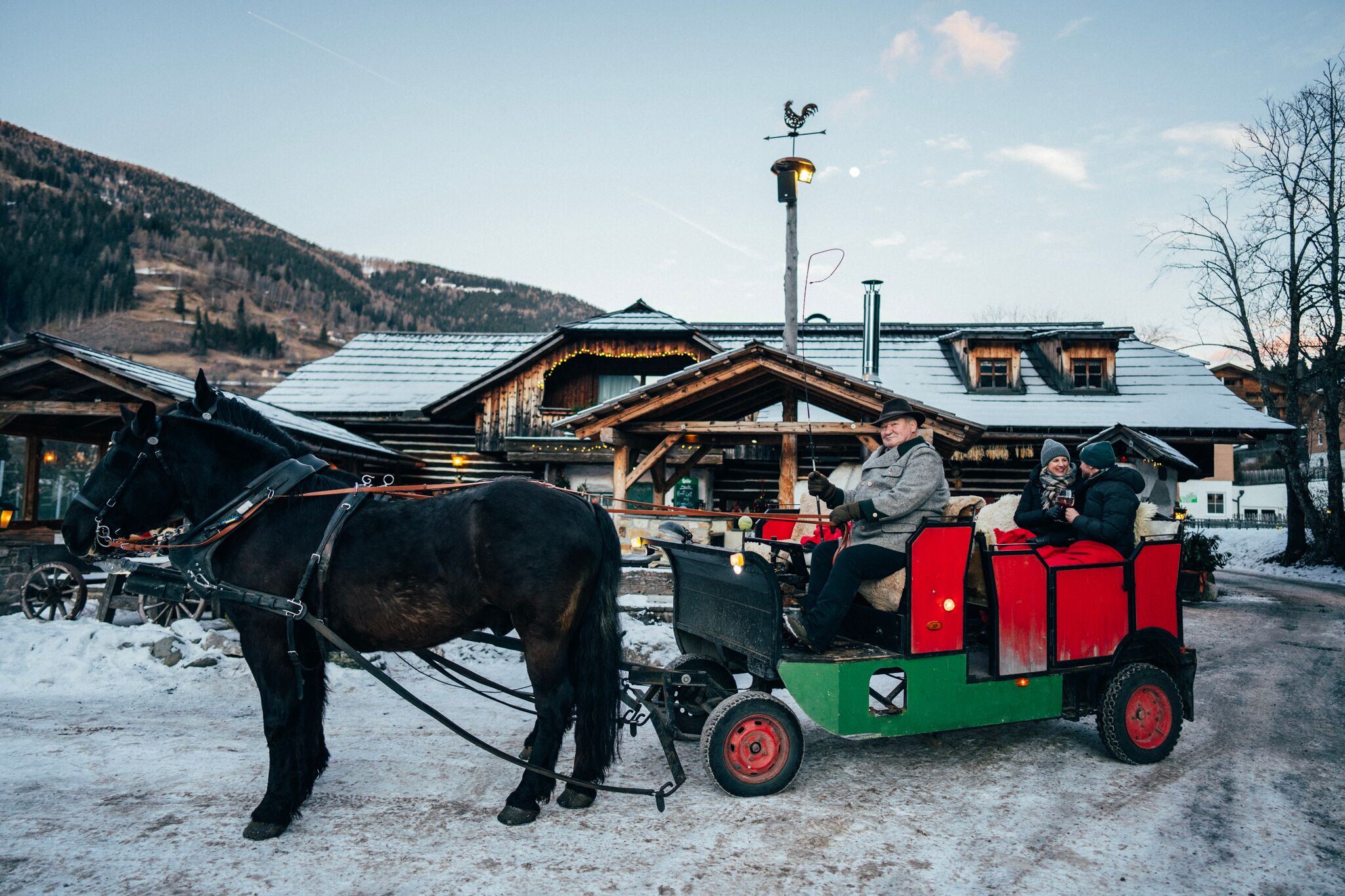 Horse-drawn carriage in front of snow-covered chalets with guests and coachman in a wintry landscape.