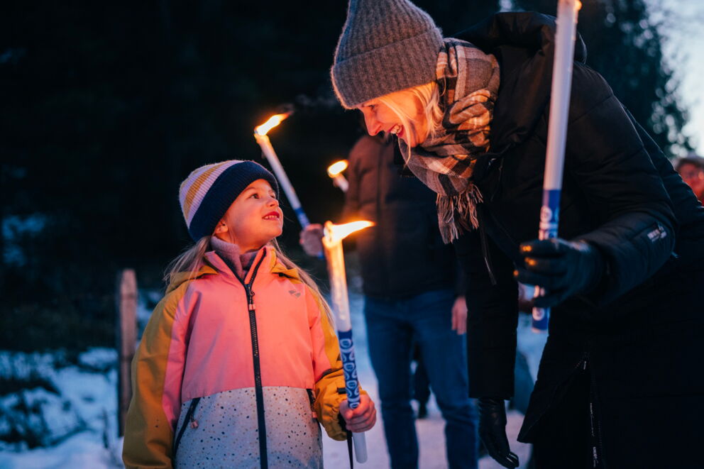 Child and adult with torches on a winter hike at dusk.