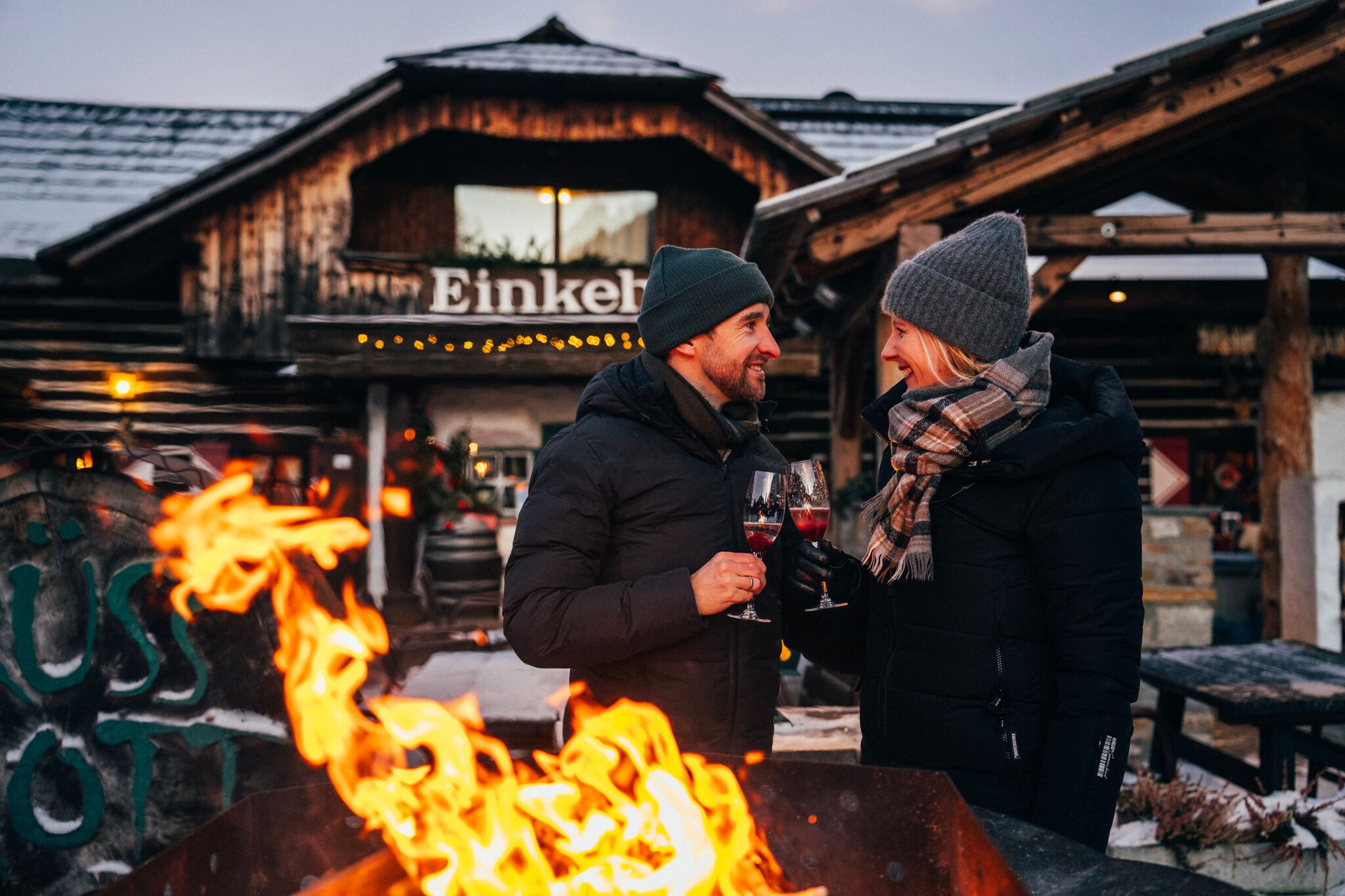 Coppia che si gode un drink davanti a un fuoco scoppiettante in un rifugio rustico.