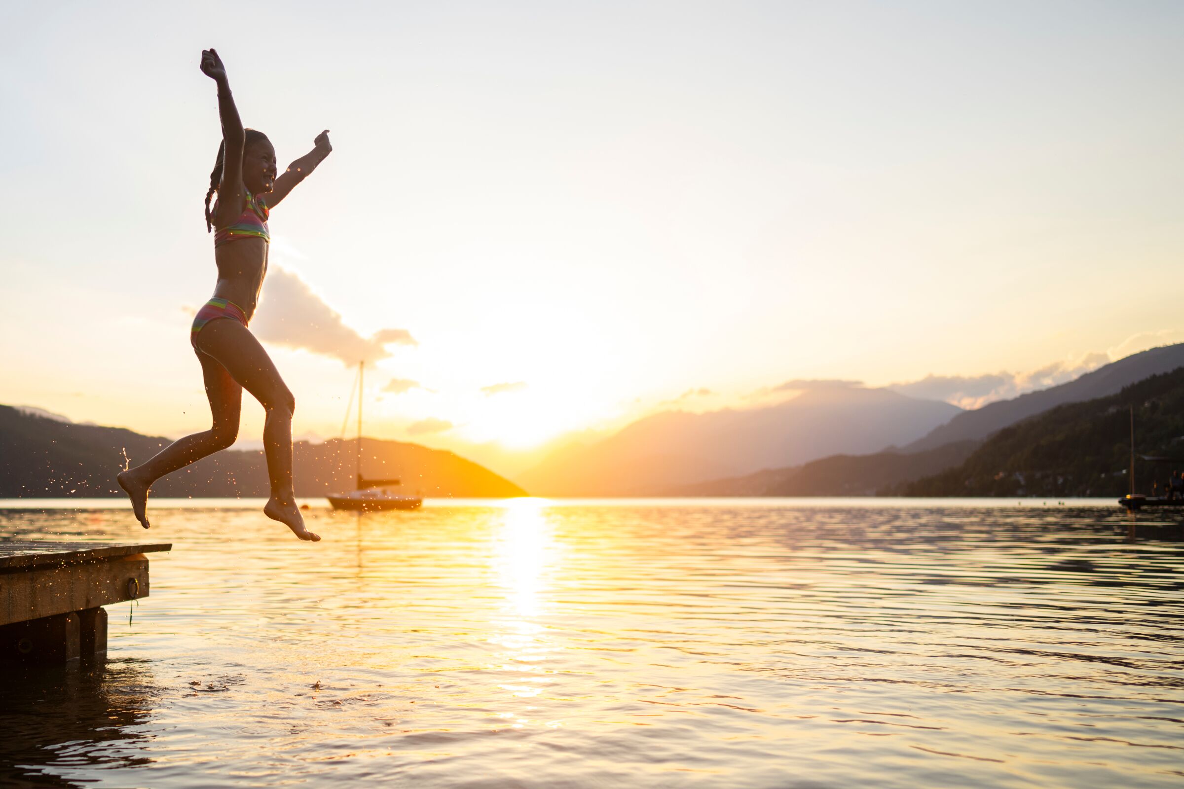 Child jumping from the jetty into the lake at sunset, mountains in the background.