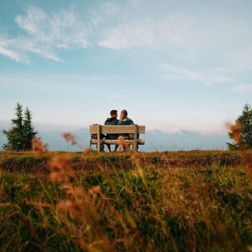 Paar sitzt auf Bank, genießt Bergblick und friedliche Naturkulisse.