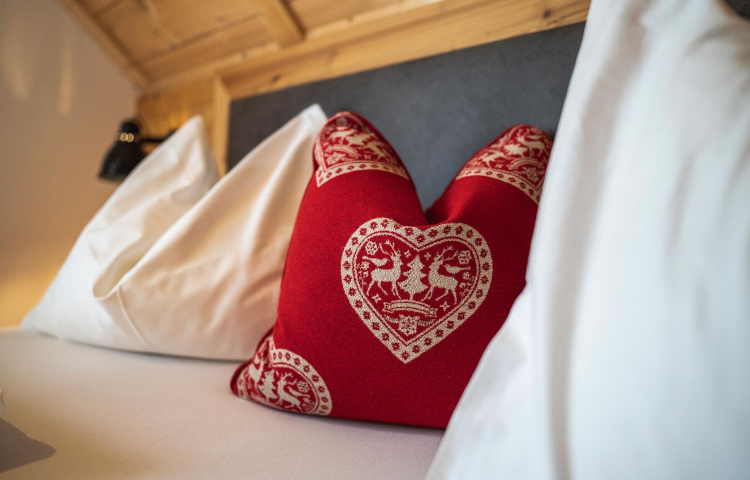 Cuscino a cuore rosso e cuscini bianchi su un letto accogliente nello chalet.