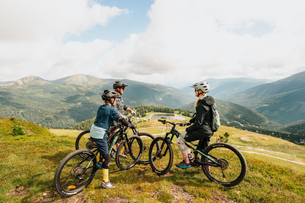 Familie genießt Mountainbike-Tour in den malerischen Kärntner Nockbergen mit weitem Ausblick.