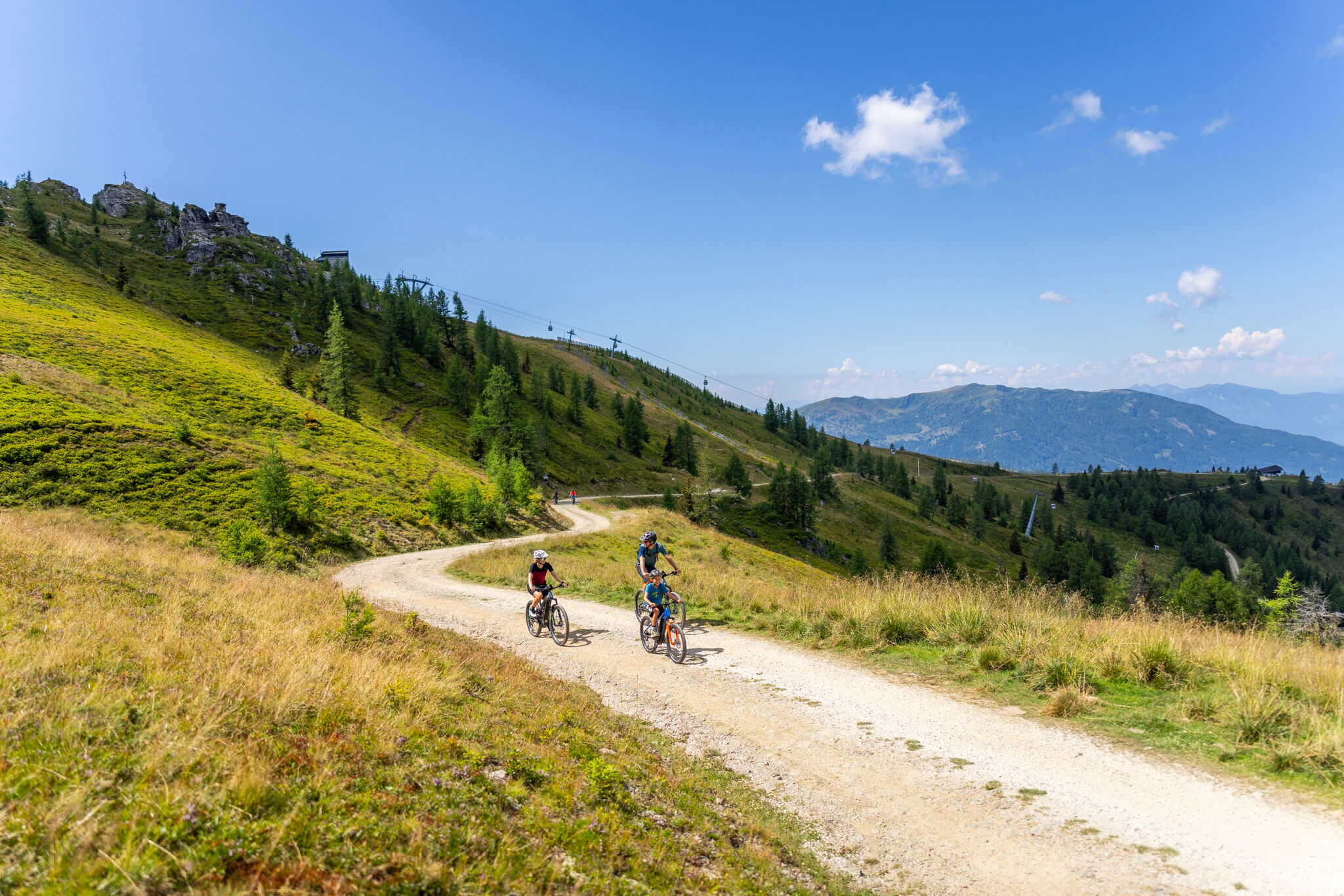 Tre ciclisti su un sentiero di montagna soleggiato e tortuoso in un paesaggio meraviglioso.