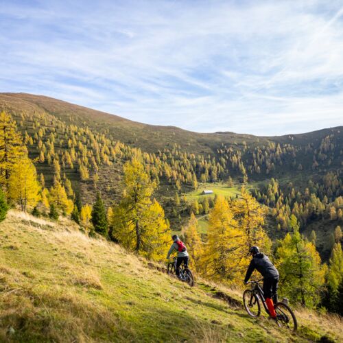 Two cyclists enjoy a ride through the autumnal landscape of the Nockberge mountains.