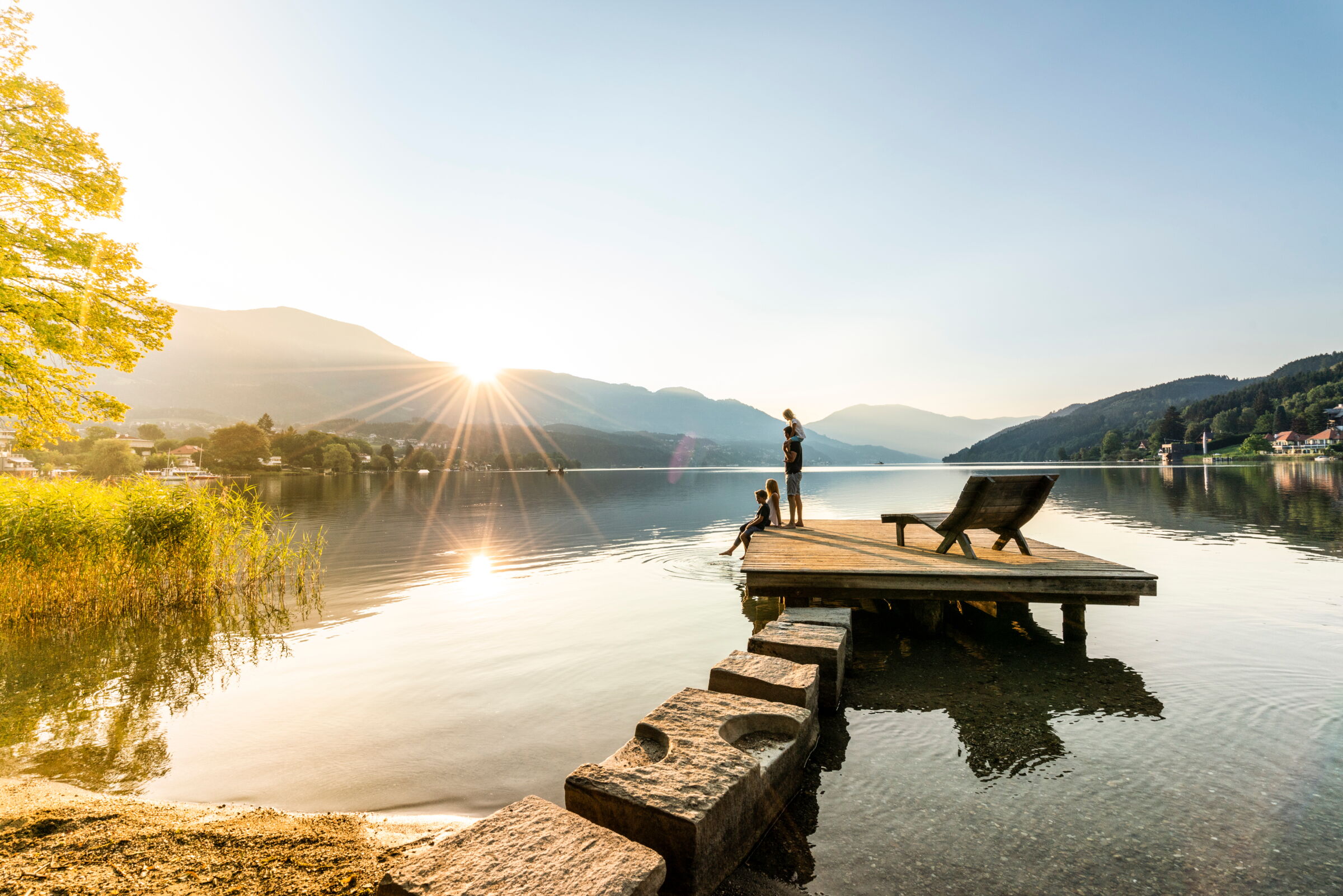 Family enjoying the sunset on a jetty by the tranquil lake.