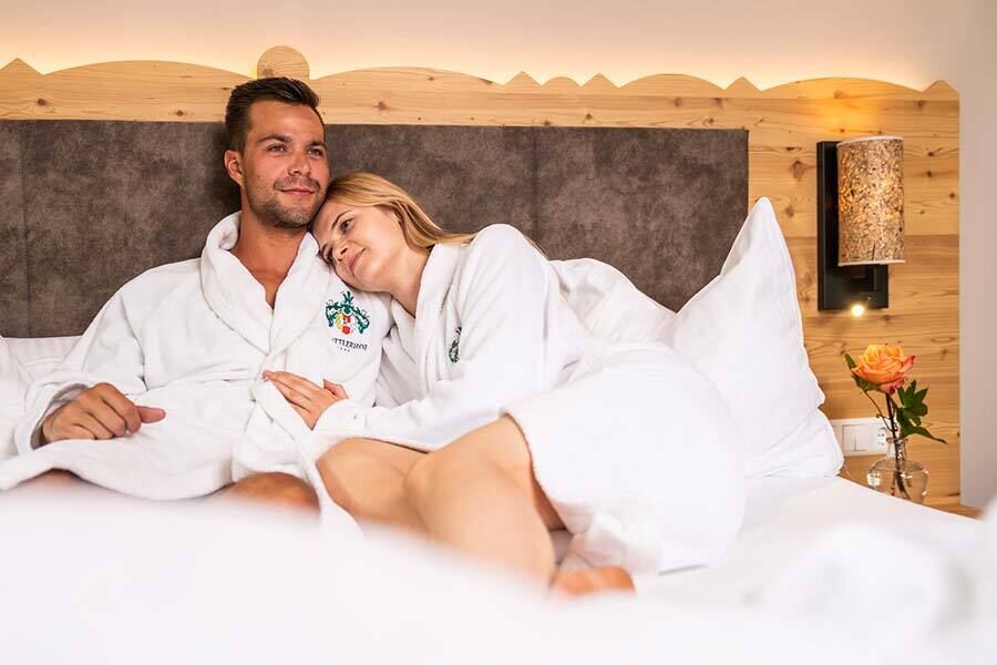 Couple in fluffy bathrobes snuggling up in a cozy chalet bed.
